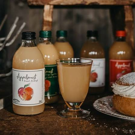 Bergströms äppelmust på flaska bredvid ett glas must och en semla på ett rustikt träbord